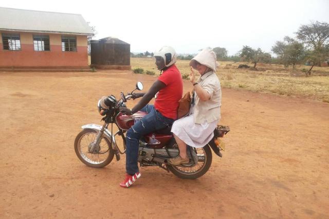 A photo of a man and a woman on a motorcyle; the man is driving, the woman is seated behind him and is waving.