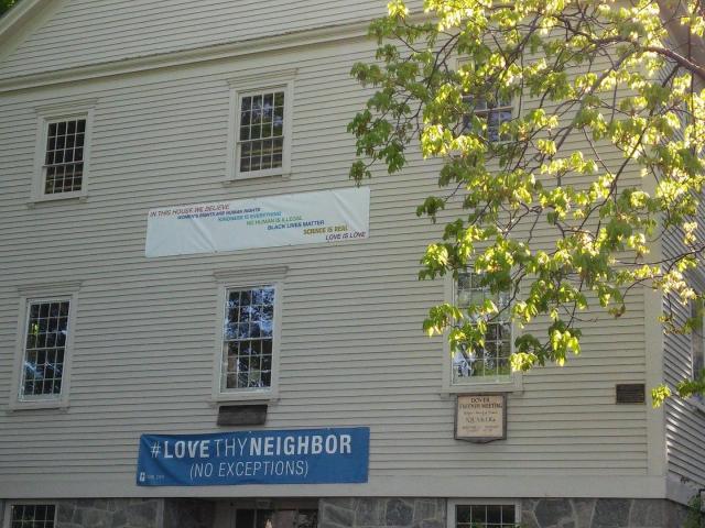Photo shows one side of Dover Friends meeting house with "Love thy Neighbor" banner