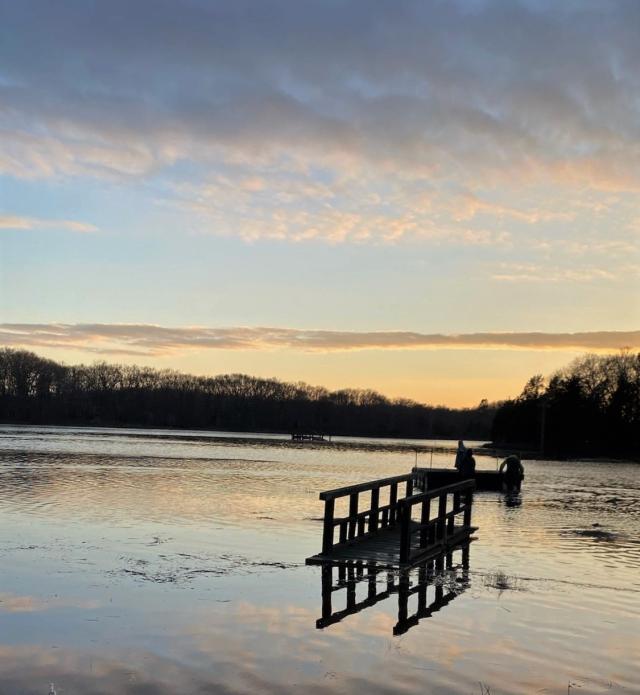 Silhouettes of two people moving a dock into the water as darkness falls