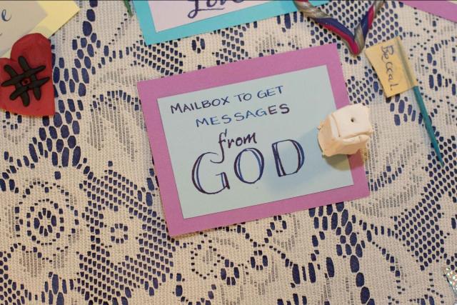A label reading "Mailbox to get messages from God" laid on a lace-covered table