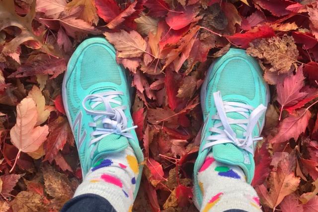 View looking downward at a pair of feet in turqoise shoes standing in fall leaves