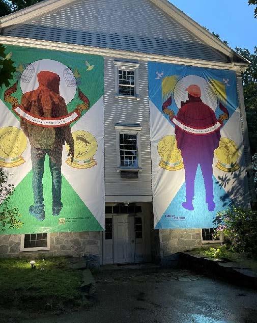 Two large banners with artwork by immigrants to the U.S. hang on the side of a meetinghouse