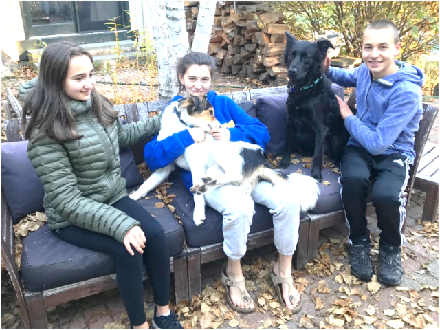 Image of three children and two dogs sitting outdoors on lawn furniture.