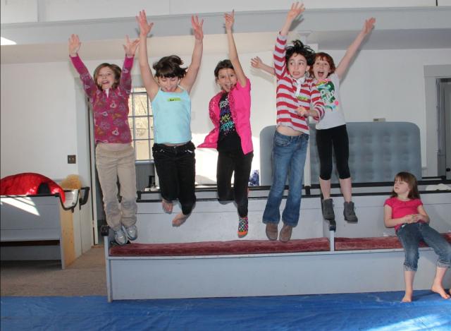 A photo of four children jumping in the air while another child sits and watches