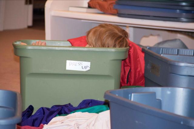 A photo of a red-headed child sitting in a plastic storage box, with just the top of his head showing