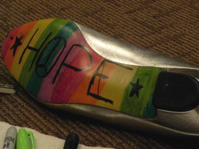 Photo shows a shoe on its side; the sole has the word "Hope" and bright colored stripes painted on it