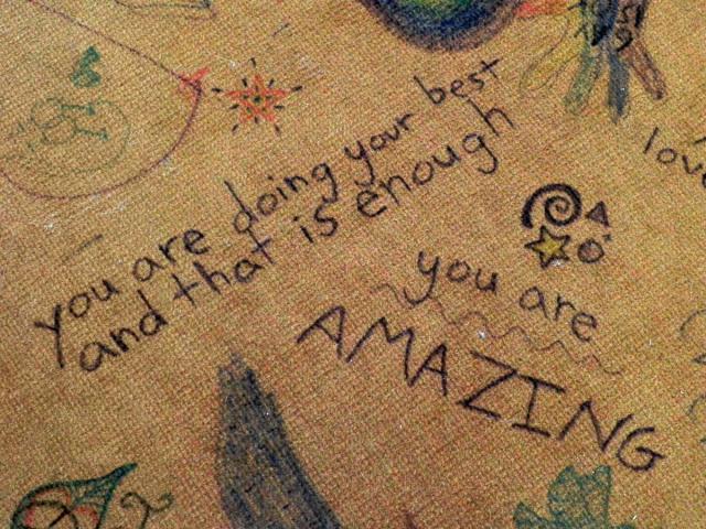 Photo shows drawings and messages on old carpet and one message reads you are doing your best and that is enough