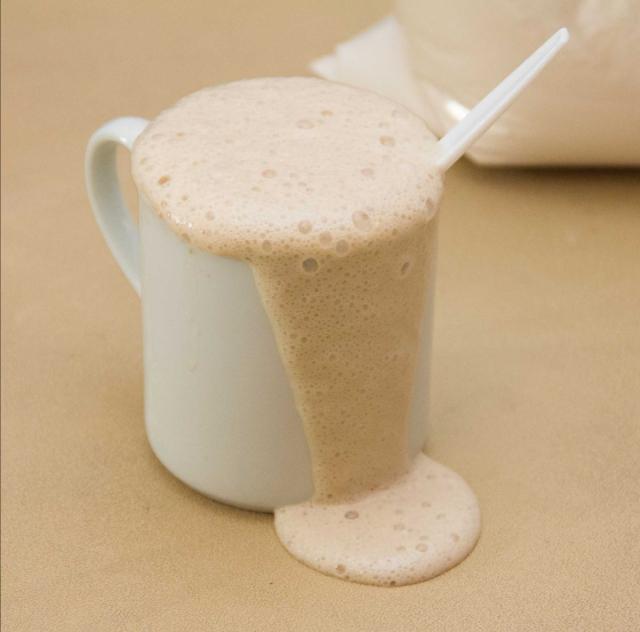 Photo of a white mug overflowing with a beige foaming yeast mixture