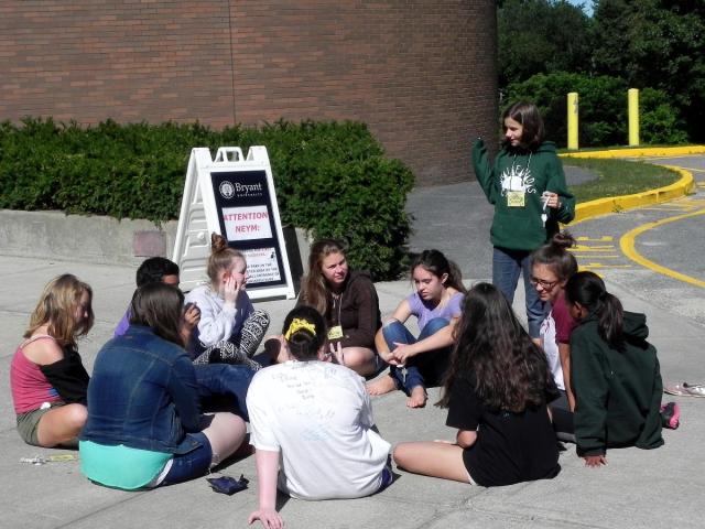 The image is of a group of teenagers sitting on the ground in a circle