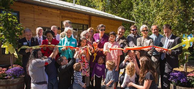 A group of adults and children cut a ribbon in front of a building