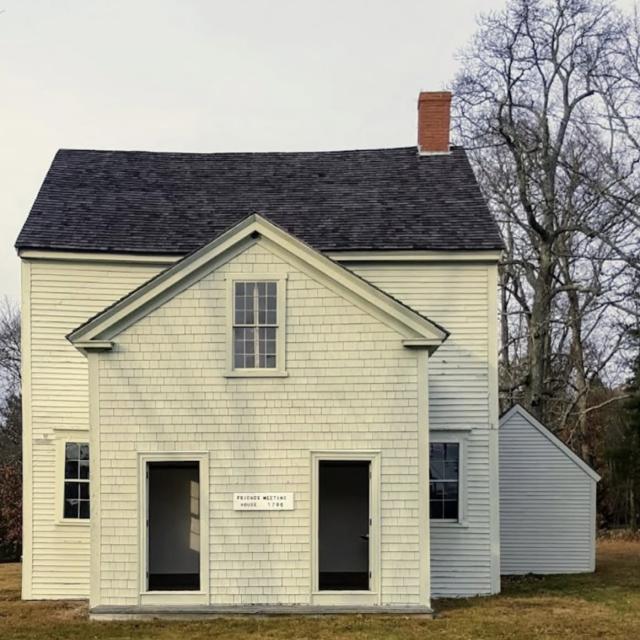 Photograph of an old Quaker meetinghouse, white with black roof, a chimney, and two entry doors