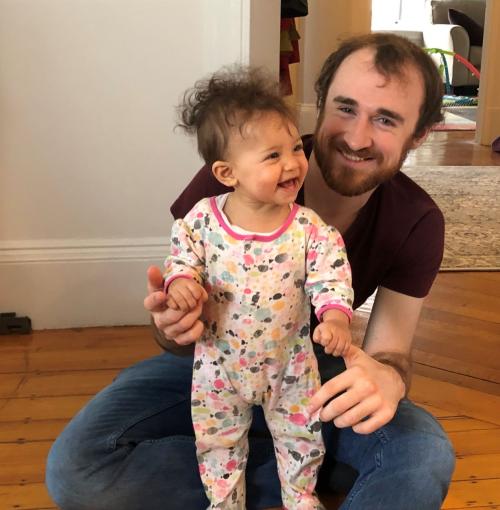 Rainer sitting on floor with young child standing in front of him.