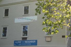 Photo shows one side of Dover Friends meeting house with "Love thy Neighbor" banner