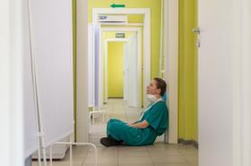 The image is female nurse wearing green scrubs sitting on the floor of a hospital corridor
