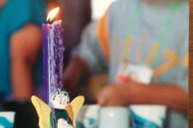 A purple candle in a ceramic candle holder shaped like an angel