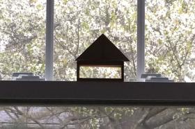 A view of a window which has a small wooden model of a building perched on the sill