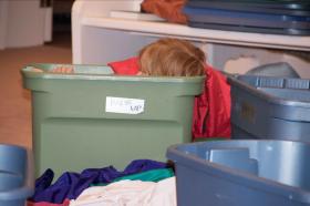 A photo of a red-headed child sitting in a plastic storage box, with just the top of his head showing