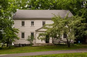 View of the Dover Friends meetinghouse, a 2-story building painted beige with a double entry.