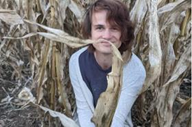 A photo of a young man seater in a field of dried cornstalks