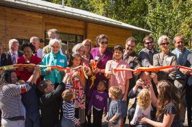 A group of adults and children cut a ribbon in front of a building